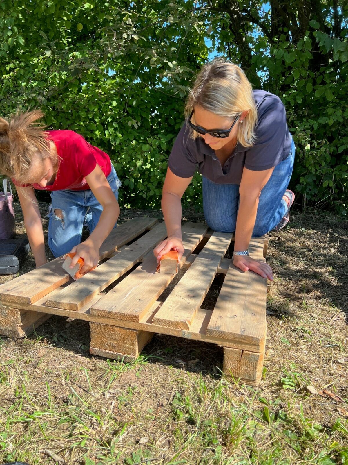 Zwei Frauen schleifen eine Holzpalette im Freien.
