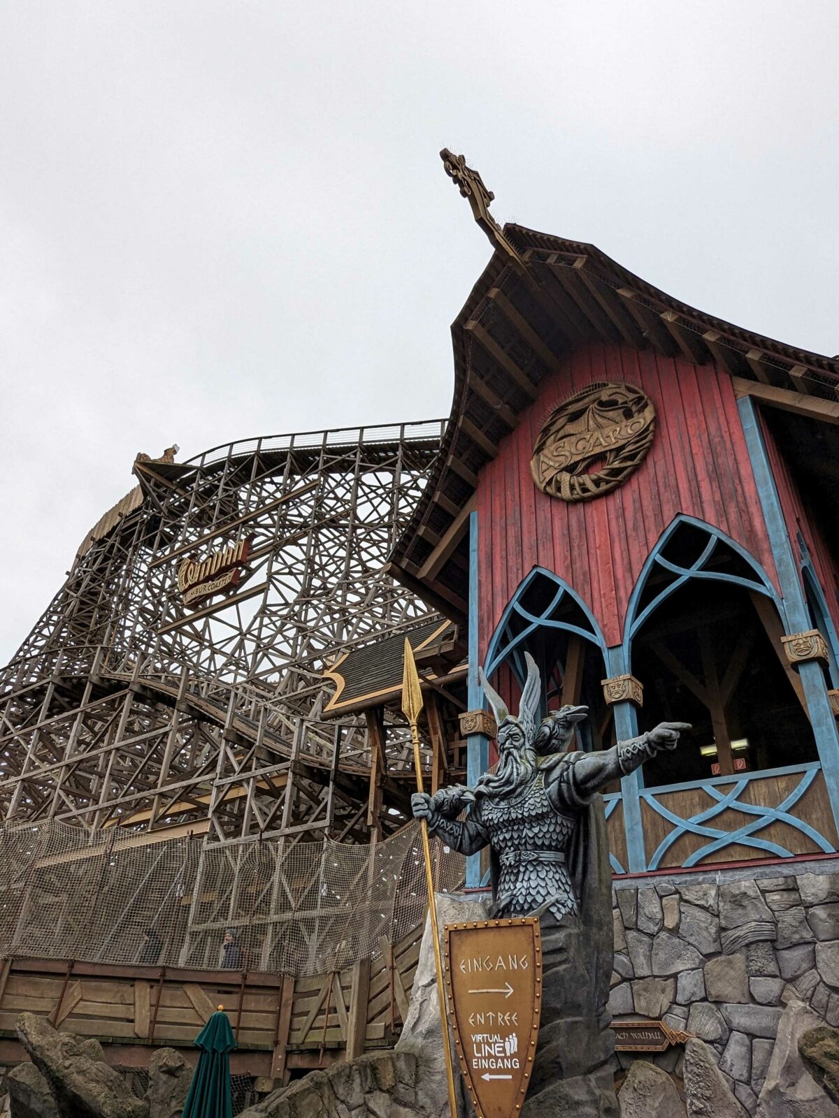 Eingangsbereich der Holzachterbahn Wodan im Europa-Park, mit einer großen Wikingerstatue und einem rot-blauen Gebäude im Vordergrund.