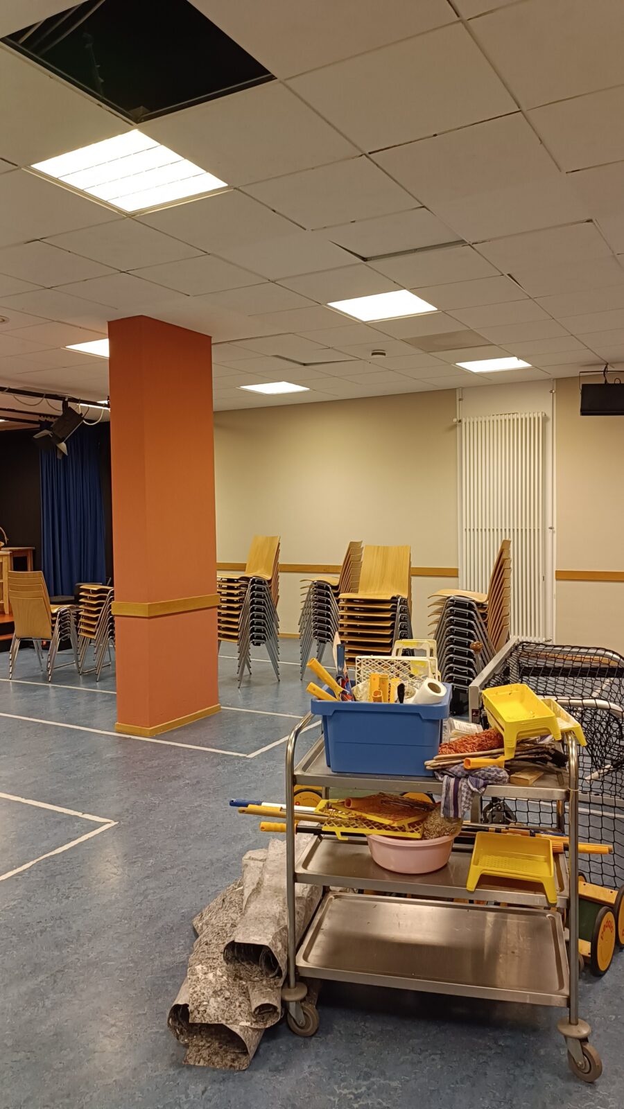 Das Bild zeigt eine Sporthalle mit frisch gestrichenen beigen Wänden. Rechts im Bild ist ein Rollwagen, mit Streichutensilien, wie Pinseln.