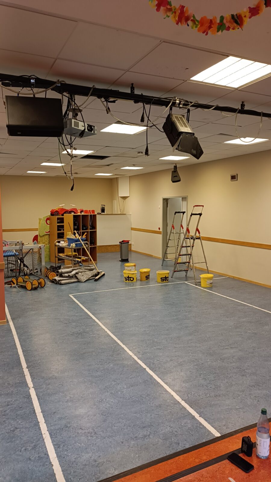 Das Bild zeigt eine Sporthalle, dessen Wände gerade frisch beige gestrichen wurden. Auf dem Boden stehen noch ein paar Farbeimer und Streichutensilien.