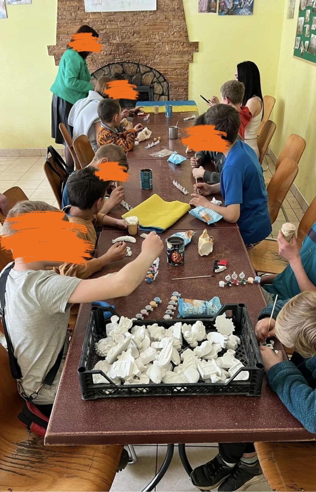 Mehrere Kinder und Erwachsene sitzen an einem großen Tisch und basteln mit verschiedenen Materialien. Sie gestalten kreative Werke und arbeiten konzentriert.