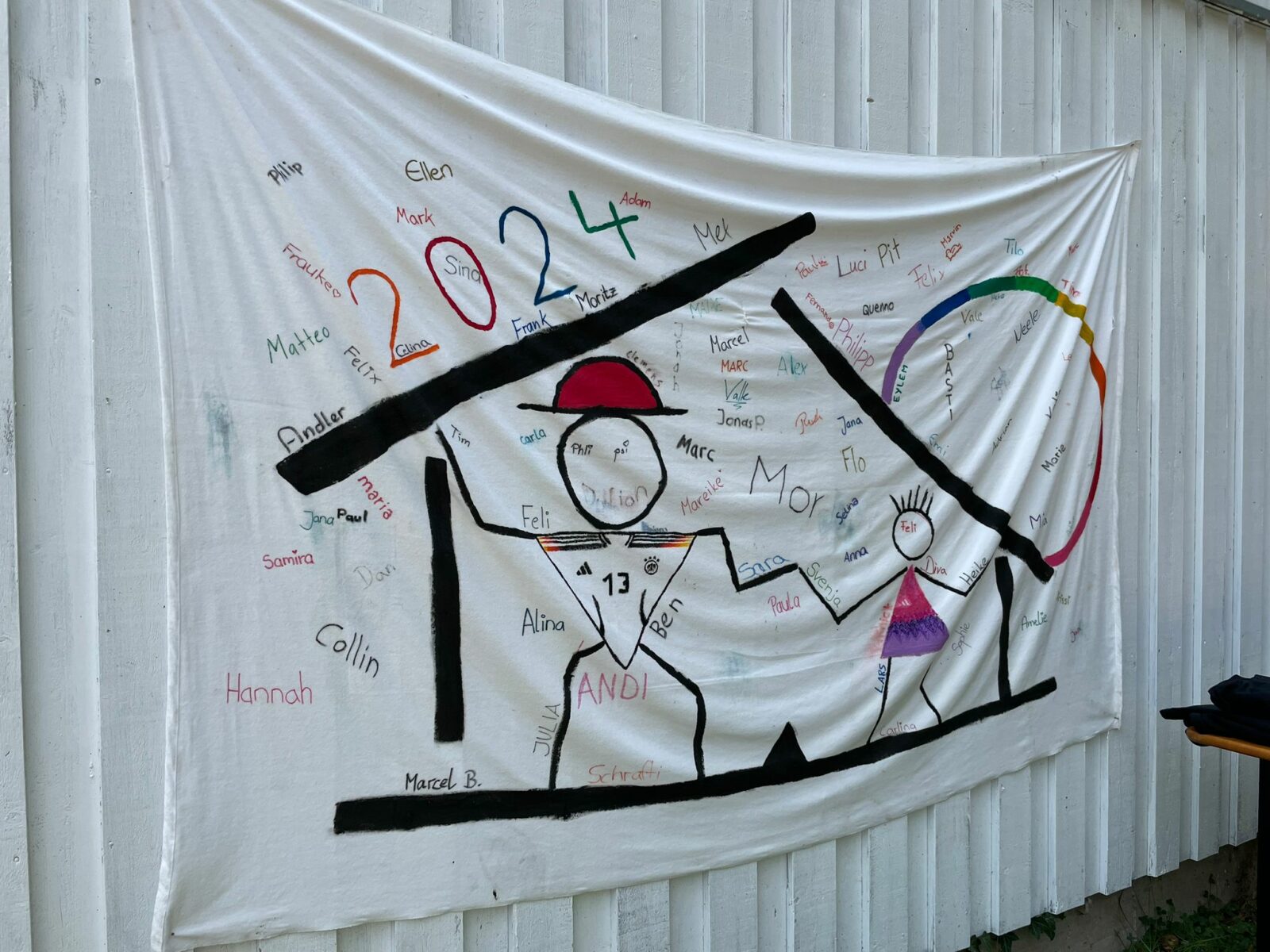 Ein weißes Lacken hängt an einem weißen Container. Auf dem Lacken sind Zeichnungen von Fußballer-Strichmännchen und darüber steht "2024". Zudem sind einige Unterschriften drauf verewigt.
