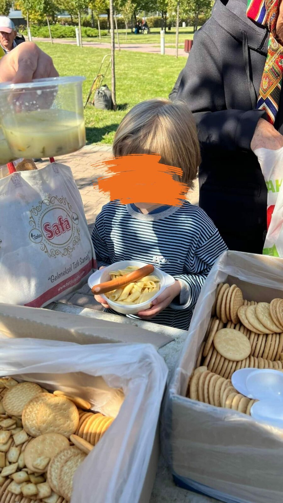 Ein kleiner Junge steht lächelnd vor einem Tisch mit einem Buffet und nimmt sich mit seinem Schälchen etwas von den Sachen.