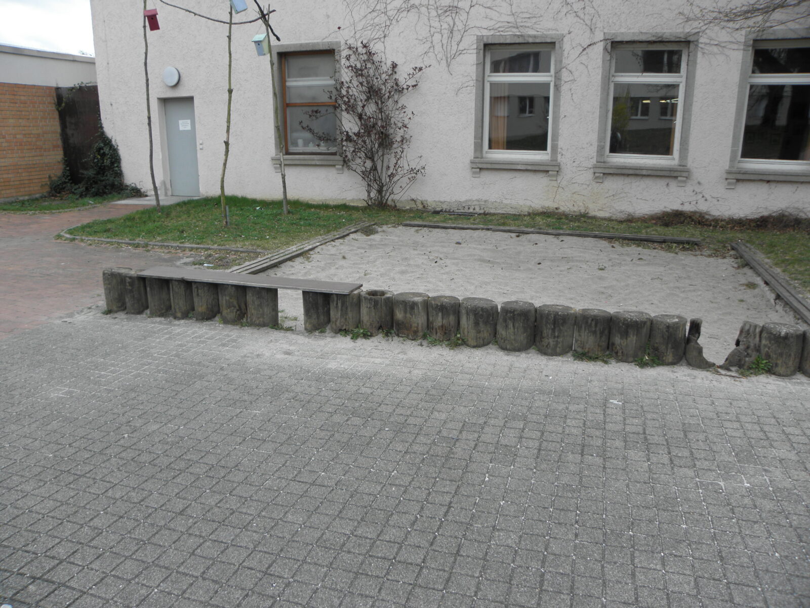Trister Sandspielkasten vor einem Gebäude.
