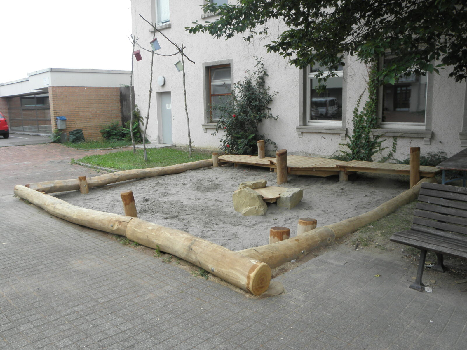 Sandspielkasten nach der Verschönerung. Um den Kasten sind jetzt Holzbaumstämme zur Verschönerung.