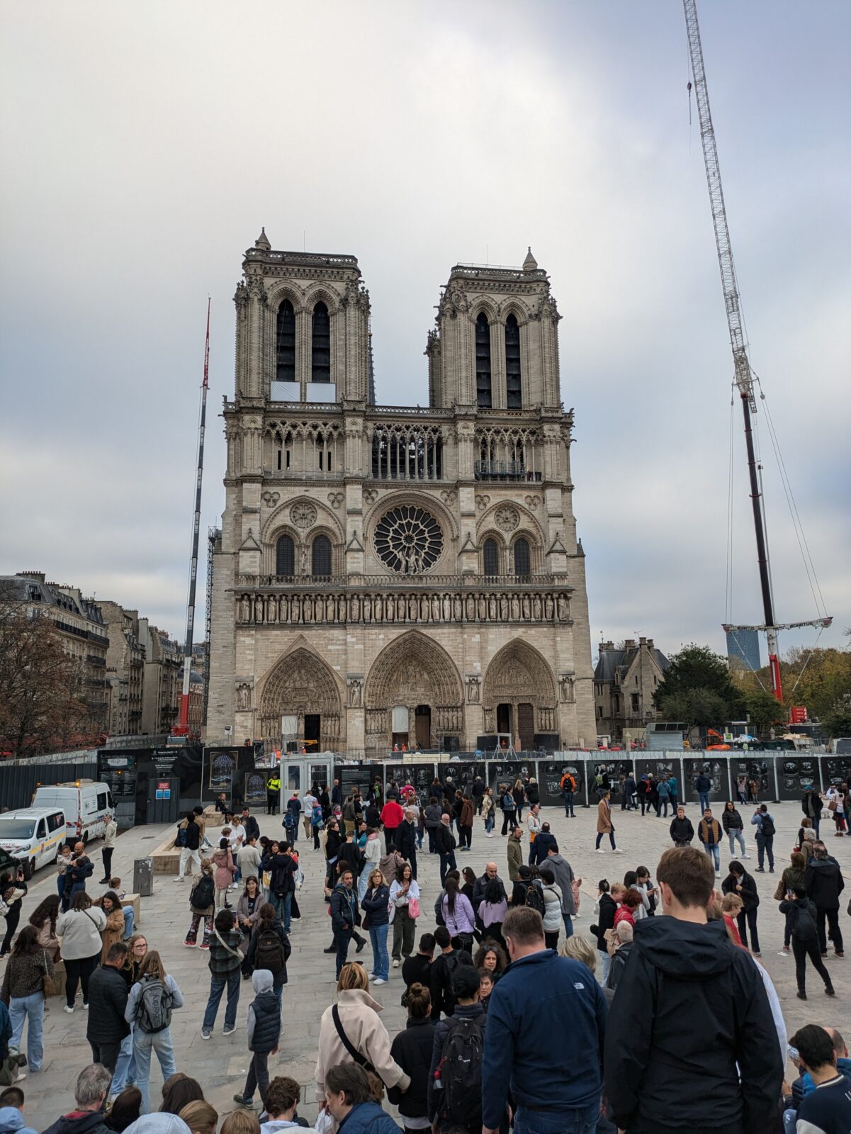 Das Bild zeigt die Notre Dame in Paris. Rechts und links neben der Notre Dame sind Krane und drumherum wurde die Kathedrale wegen der Baustelle abgesperrt. Auf dem Vorplatz sieht man viele Menschen, die mit ihren Smartphones Fotos von der Kathedrale machen.