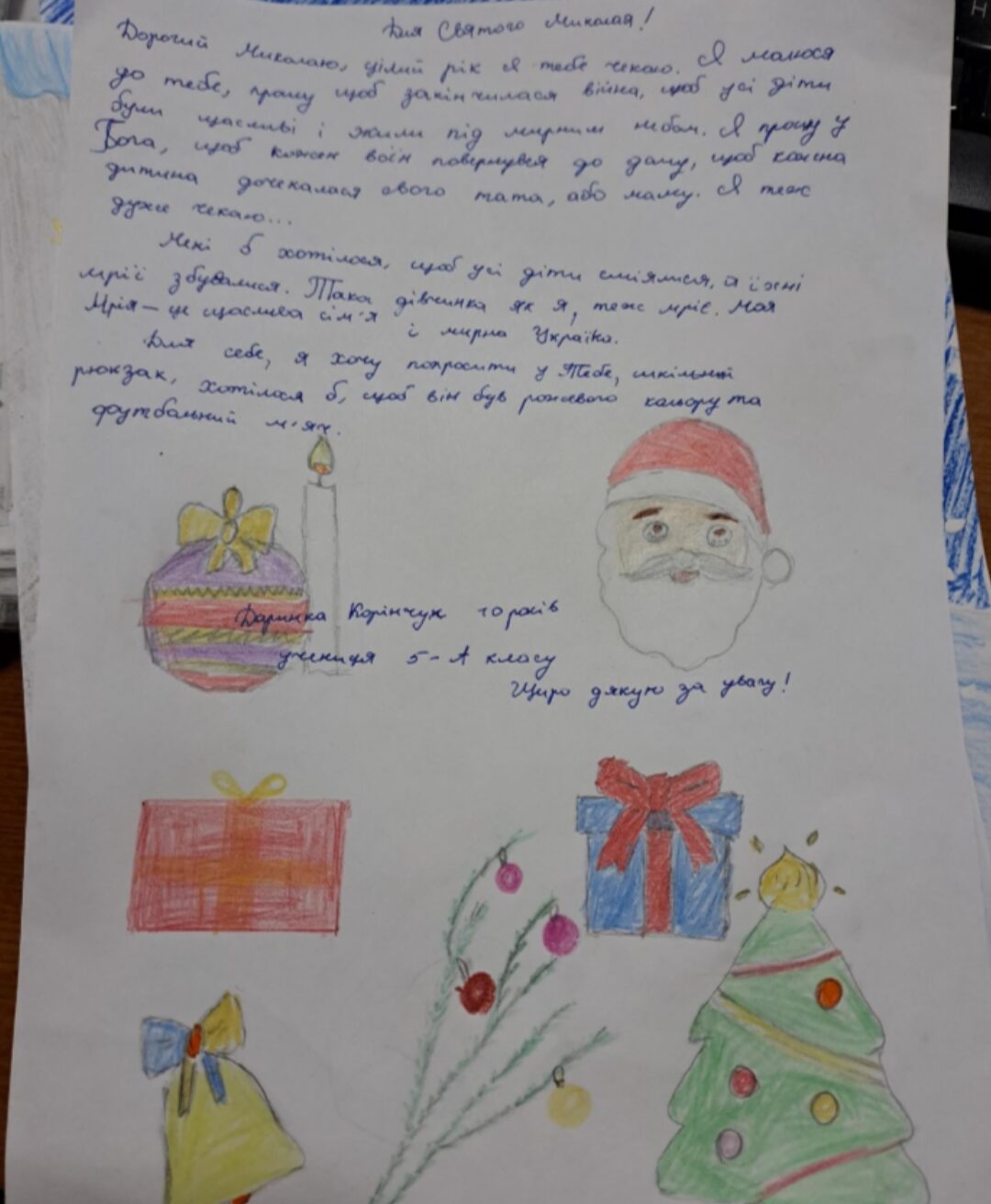 Handgeschriebener Brief mit bunten Zeichnungen, darunter ein Weihnachtsbaum, Geschenke und Christbaumschmuck. Der Text ist in ukrainischer Sprache verfasst und scheint eine Botschaft an den Heiligen Nikolaus zu sein, in der Wünsche und Hoffnungen ausgedrückt werden. Die Zeichnungen sind liebevoll gestaltet und vermitteln eine festliche Atmosphäre.