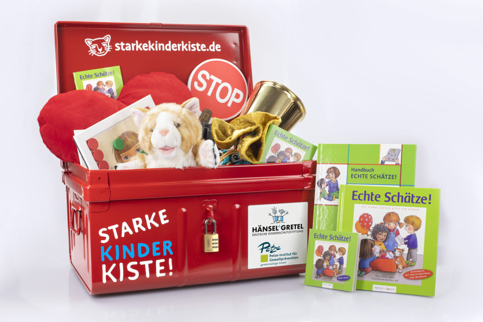 Ein roter Metallkoffer mit der Aufschrift „Starke Kinder Kiste!“ ist geöffnet und enthält verschiedene Materialien wie Bücher, ein Stoffherz, eine Plüschkatze und weitere Gegenstände. Neben dem Koffer sind grüne Bücher mit dem Titel „Echte Schätze!“ zu sehen, die sich mit Gewaltprävention und Kinderrechten beschäftigen. Der Koffer ist Teil eines Projekts der Deutschen Kinderschutzstiftung Hänsel + Gretel und des Petze-Instituts.