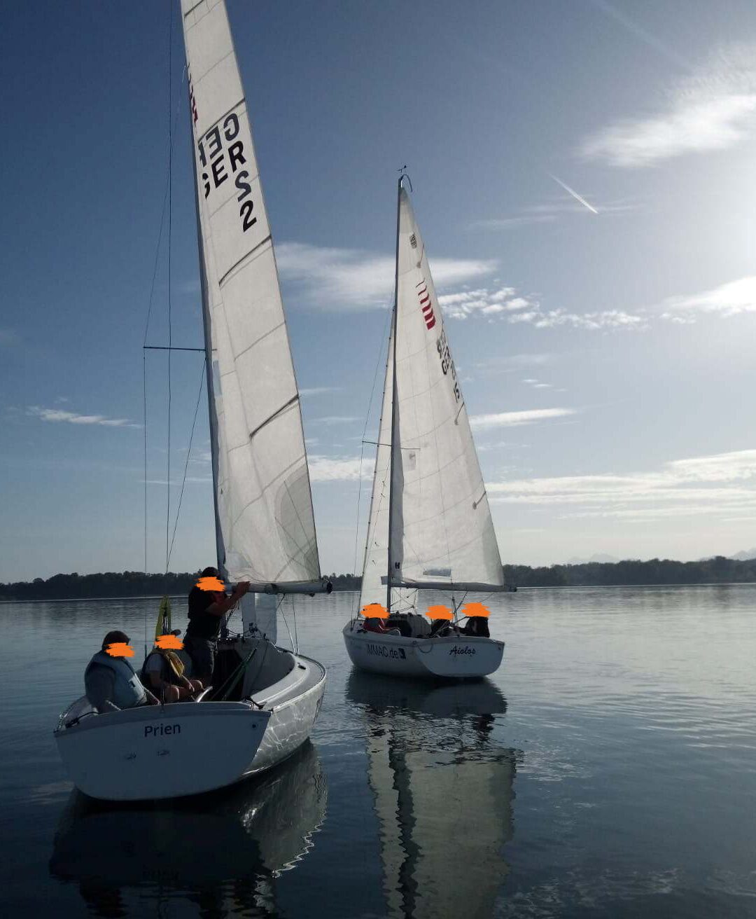 Zwei Segelboote schwimmen auf dem Wasser. Die Boote sind weiß und die Segel sind ebenfalls weiß. Auf den Segeln stehen die Buchstaben G, E, R und S. Die Gesichter der Besatzungsmitglieder sind verpixelt.
