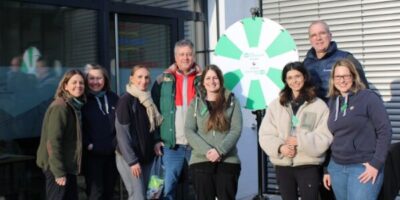 Eine Gruppe von fünf Frauen und zwei Männern stehen vor einem Gebäude mit Glasfront. Die Gruppe besteht aus vier Frauen und einem Mann. Die Frauen tragen Jacken und Schals, der Mann eine grüne Jacke. Sie alle lächeln in die Kamera.