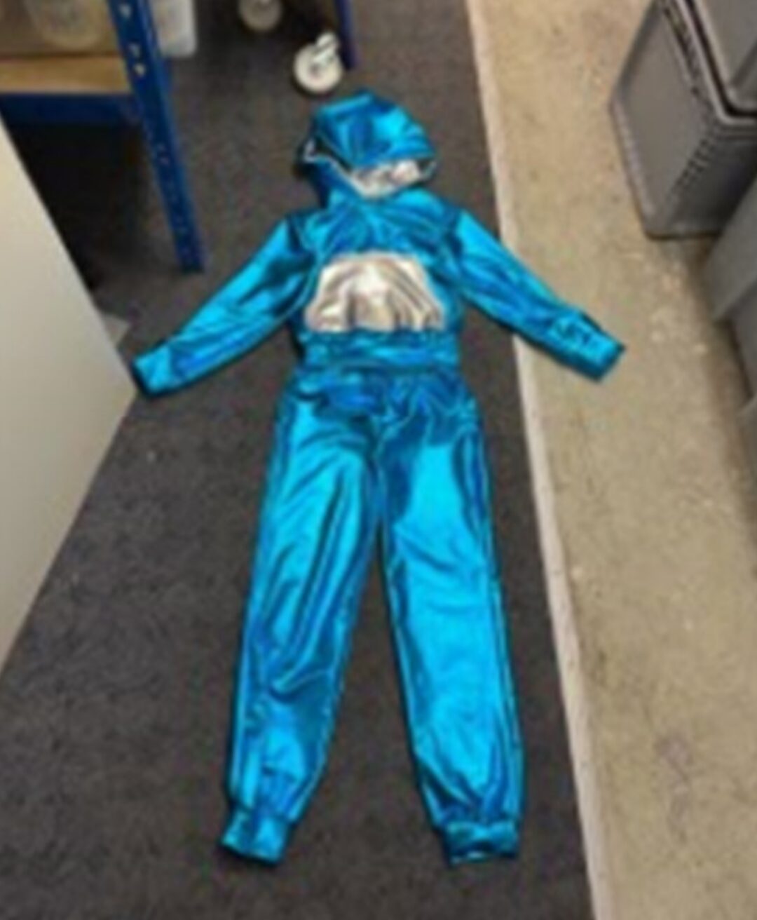 Ein blauer ganz Körper Kinderanzug, der auf dem Boden liegt. Er hat eine Kapuze und schimmert.
