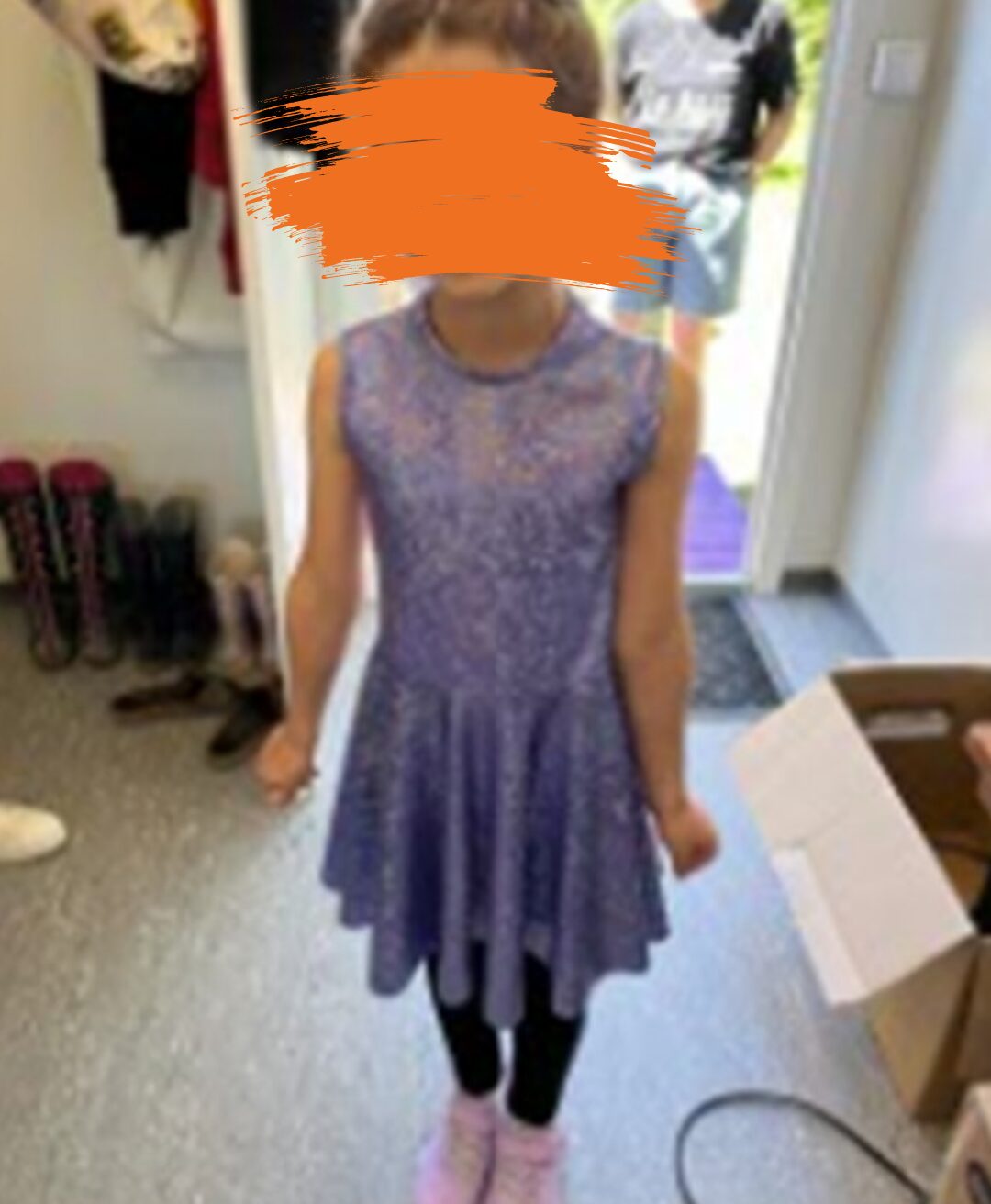 Ein Mädchen trägt ein lilafarbenes, schimmerndes Kleid. Sie trägt einen hohen Dutt und steht selbstbewusst vor der Kamera.