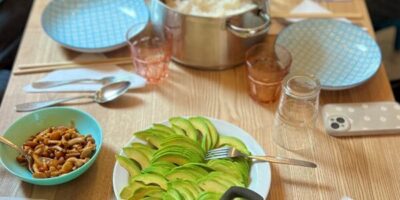 Ein gedeckter Tich mit Tellern und Schüsseln. In den Schüsseln scheinen Zutaten für eine Bowl zu sein, die man sich selbst zusammenstellen kann. In der Mitte des Tisches steht ein Topf mit Reis.