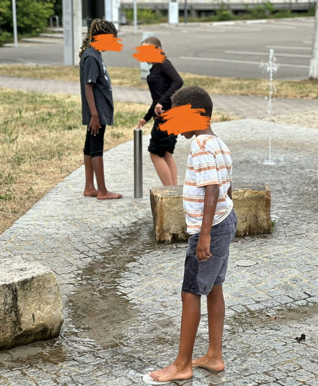 Drei Kinder spielen an einem Wasserspielplatz. Ihre Gesichter sind unkenntlich gemacht.