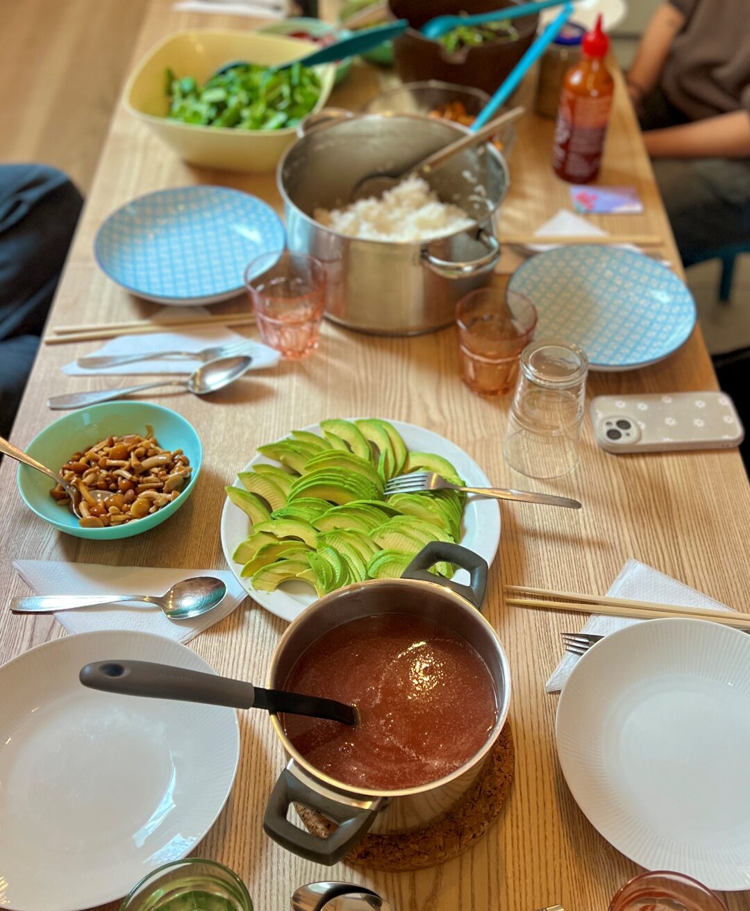 Ein gedeckter Tich mit Tellern und Schüsseln. In den Schüsseln scheinen Zutaten für eine Bowl zu sein, die man sich selbst zusammenstellen kann. In der Mitte des Tisches steht ein Topf mit Reis.