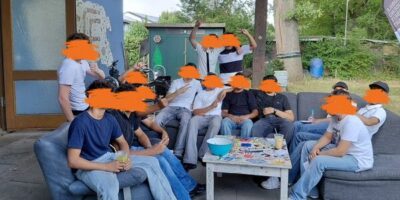 Eine Gruppe von Freunden sitzt auf einer Couch im Freien, ihre Gesichter sind unkenntlich gemacht. Sie trinken Cocktails und unterhalten sich.