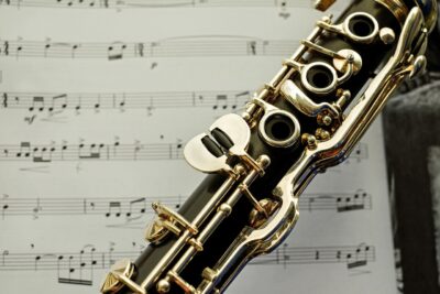 Nahaufnahme einer Klarinette vor einem Notenblatt. Die glänzenden Klappen und das schwarze Holz des Instruments sind deutlich sichtbar. Im Hintergrund sind verschwommene Noten und musikalische Zeichen zu erkennen, die eine harmonische Verbindung zwischen Instrument und Musik darstellen.
