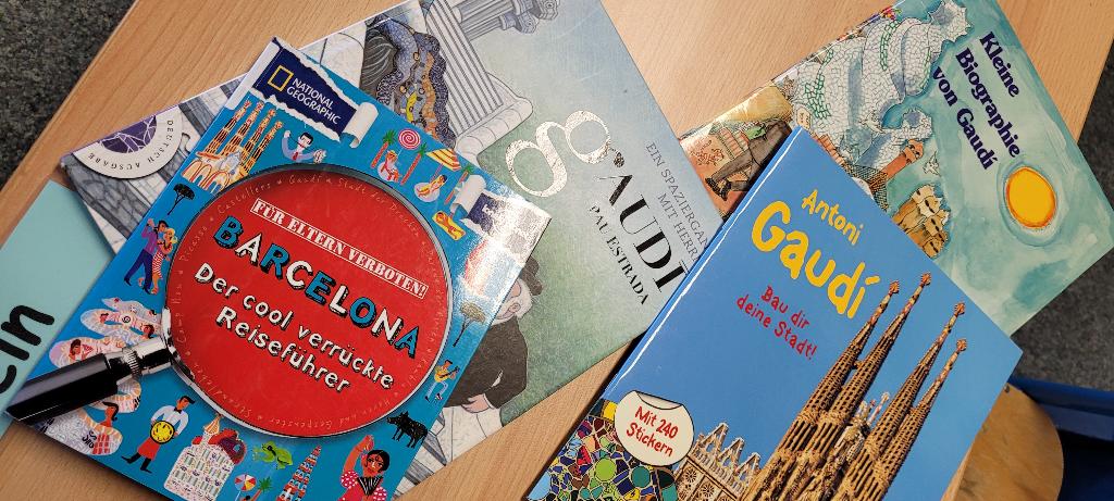Ein Stapel von Büchern über Barcelona und Antoni Gaudí liegt auf einem Tisch. Das oberste Buch ist ein Reiseführer von National Geographic mit dem Titel "Barcelona - Der cool verrückte Reiseführer". Weitere Bücher beschäftigen sich mit Gaudís Leben und Werk.