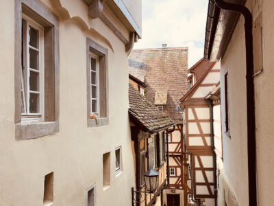 Eine enge Gasse in einer Altstadt mit Fachwerkhäusern. Die Gebäude sind dicht aneinander gebaut und strahlen historischen Charme aus. Ein paar Fenster und Türen sind sichtbar.