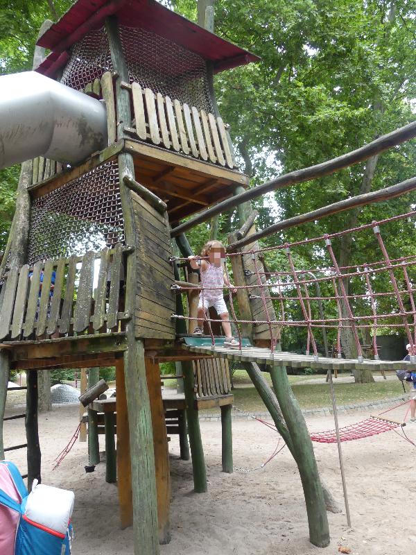 Ein Kind spielt auf einem Klettergerüst auf einem Spielplatz. Es läuft über eine Hängebrücke.