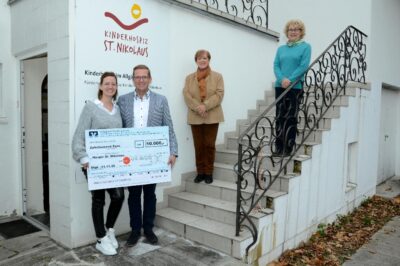 Eine Gruppe von vier Personen steht auf einer Treppe vor einem Gebäude und hält ein großes Schild. Sie posieren für ein Foto und wirken zufrieden.