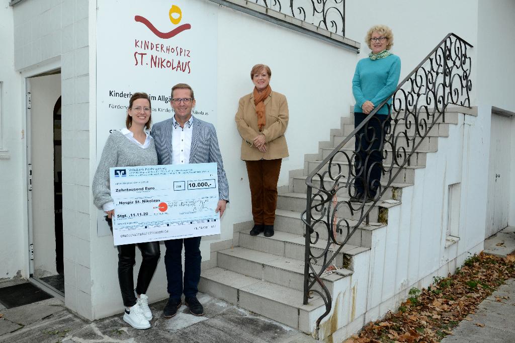 Eine Gruppe von vier Personen steht auf einer Treppe vor einem Gebäude und hält ein großes Schild. Sie posieren für ein Foto und wirken zufrieden.