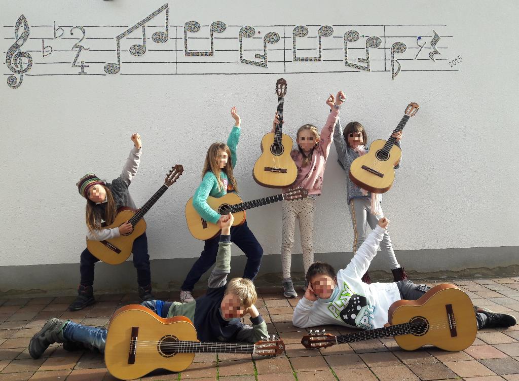 Eine Gruppe von Kindern posiert fröhlich mit Akustikgitarren vor einer Wand, die mit Musiknoten dekoriert ist. Die Kinder zeigen verschiedene kreative Posen und scheinen Spaß zu haben. Der Boden besteht aus Pflastersteinen und die Szene wirkt lebendig und musikalisch.