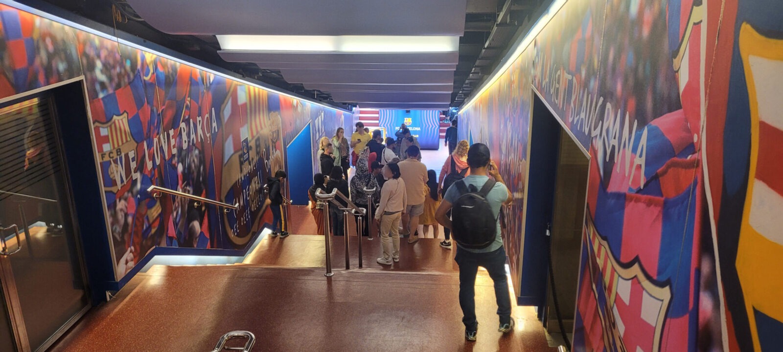Besucher betreten einen bunt dekorierten Tunnel mit FC Barcelona-Motiven und Schriftzügen im Camp Nou Stadion.