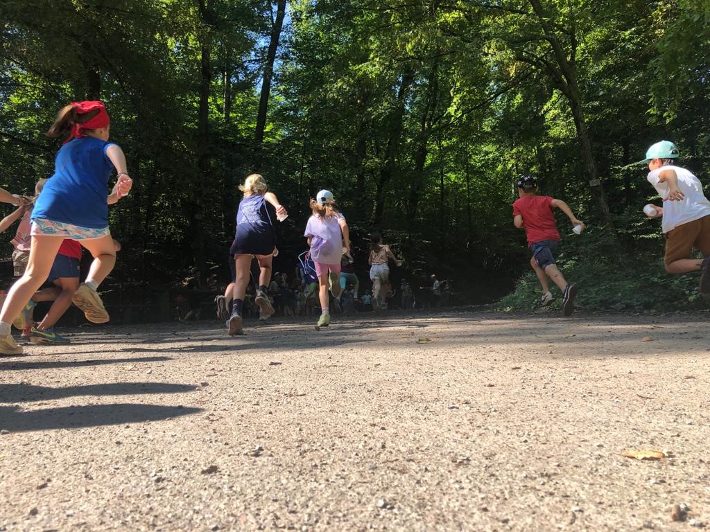 Kinder rennen auf einem Waldweg in Richtung eines schattigen Waldbereichs.