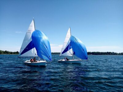 Zwei Segelboote mit blauen Spinnakern segeln auf einem See unter klarem, blauem Himmel.