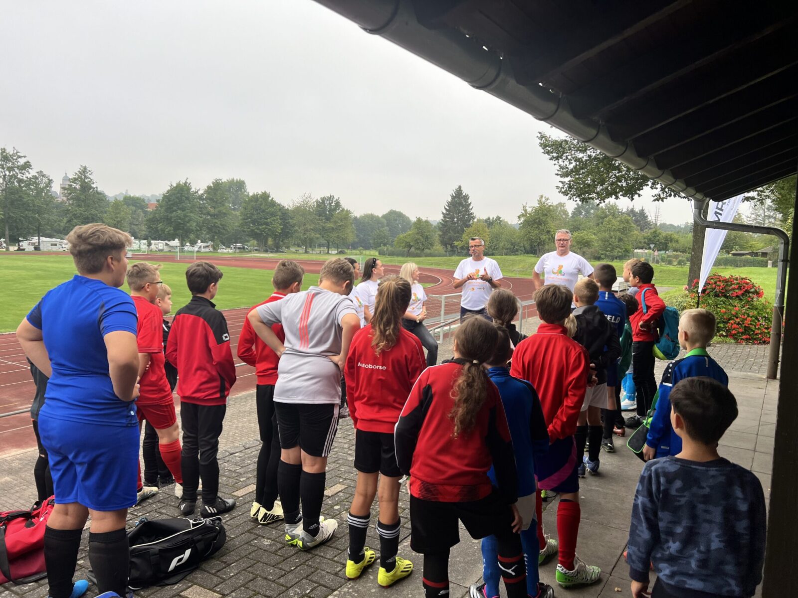 Kinder in Fuzßballklamotten stehen beisamen vor zwei Trainern.