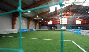Zusehen ist eine Fußballfeld in einer Sporthalle. Durch Fenster in der Decke der Halle kommt Tageslicht ins Innere.
