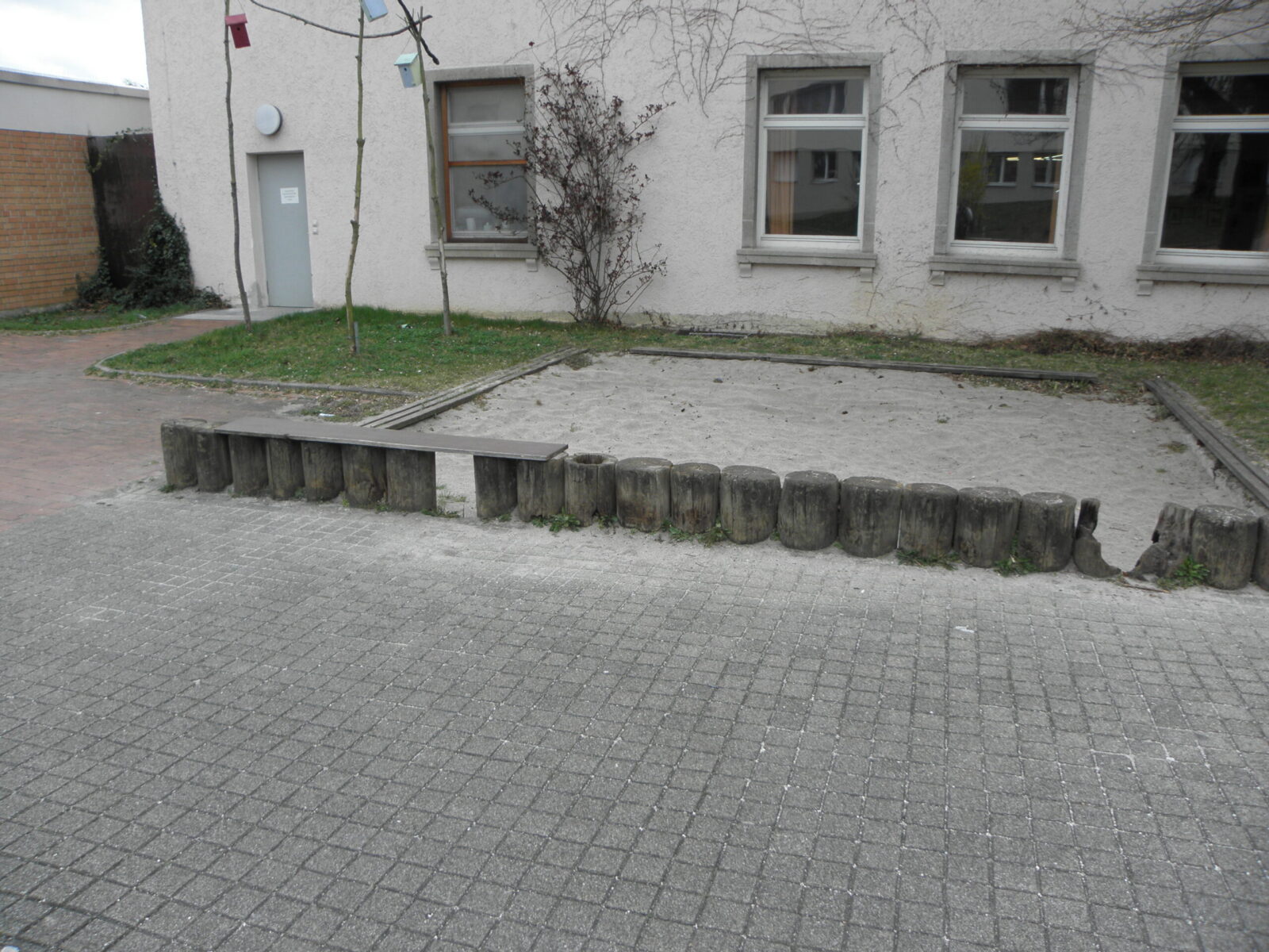 Trister Sandspielkasten vor einem Gebäude.