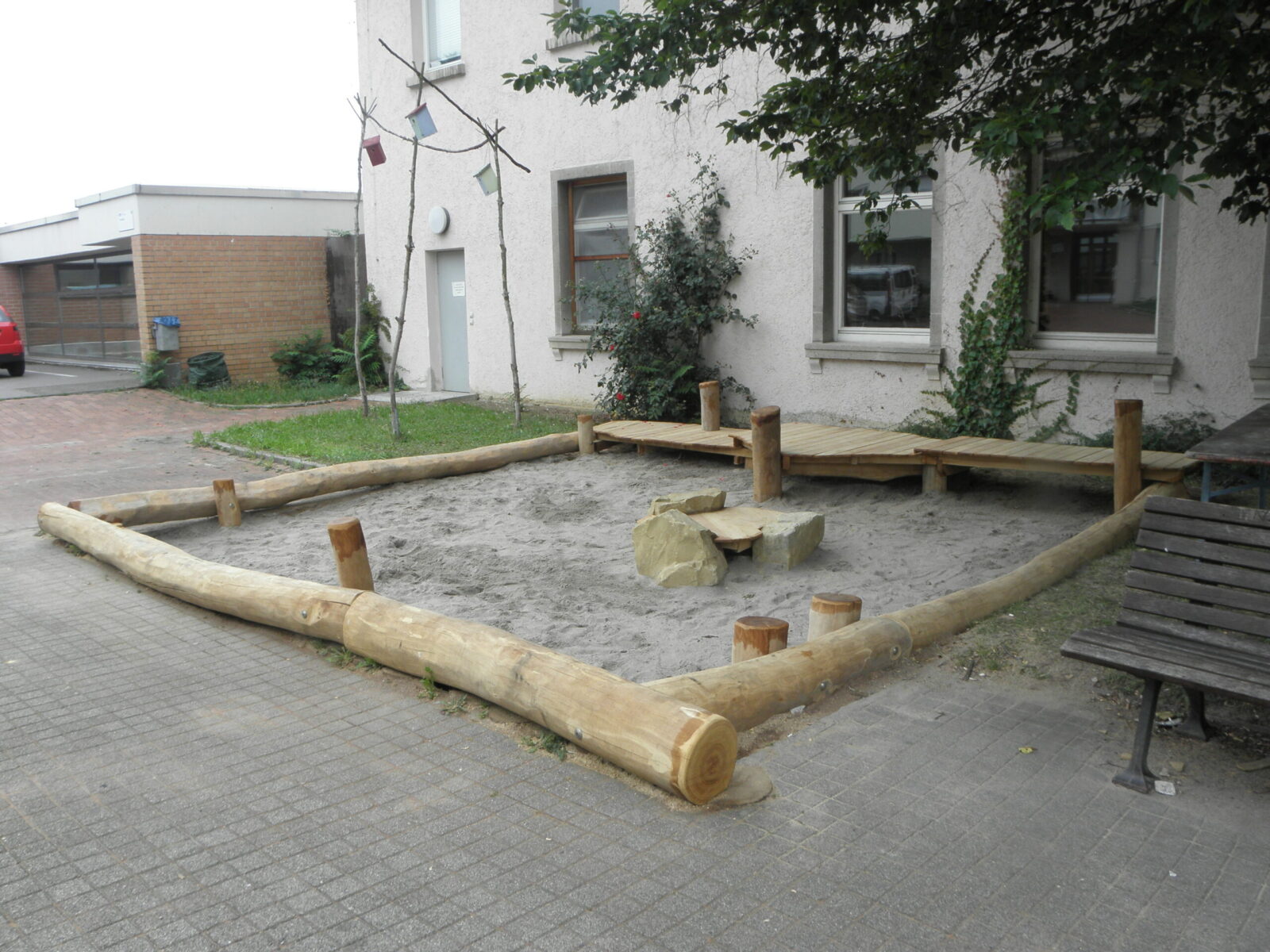 Sandspielkasten nach der Verschönerung. Um den Kasten sind jetzt Holzbaumstämme zur Verschönerung.