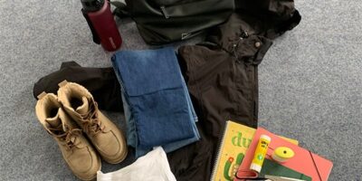 Das Bild zeigt eine Auswahl an gespendeten Gegenständen für das „MARA“-Projekt von LAGAYA e.V. Zu sehen sind ein schwarzer Rucksack, eine Wasserflasche, ein Paar gefütterte Winterschuhe, eine Jeans, ein weißes T-Shirt und eine schwarze Winterjacke. Daneben liegen Schulmaterialien wie ein Notizbuch, eine Mappe, ein Schreibblock, ein Klebestift, Schere, Marker und Textmarker. Diese Spenden sollen einer Familie helfen, die durch KINIKI unterstützt wird.