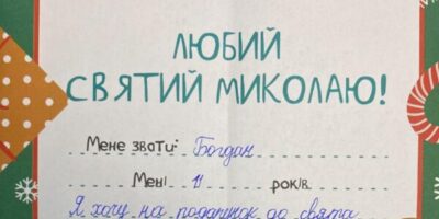 Ein handgeschriebener Brief eines Kindes an den Heiligen Nikolaus auf Ukrainisch. Der Brief ist auf einem festlichen, weihnachtlich gestalteten Papier mit grünen und roten Verzierungen sowie Illustrationen von Lebkuchenfiguren und dem Heiligen Nikolaus. Das Kind namens Bohdan, 11 Jahre alt, wünscht sich ein LEGO-Technik-Supercar und schreibt, dass es gerne mit Baukästen spielt und später Ingenieur werden möchte.